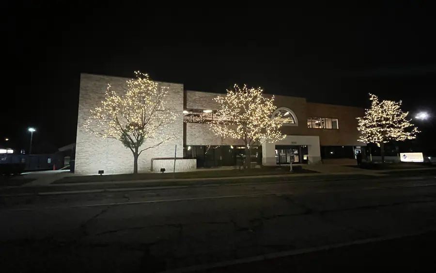 A two story brick office building at night with three trees in front fully wrapped in warm white lights.