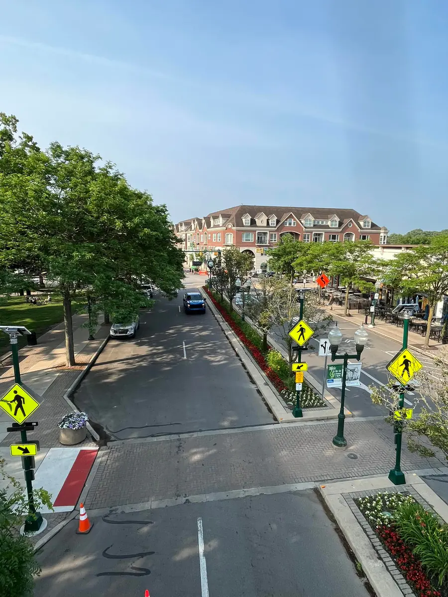 An elevated daytime view of a downtown street with pedestrian crossing signs, a planted median, street trees and a brick building at the end of the block.