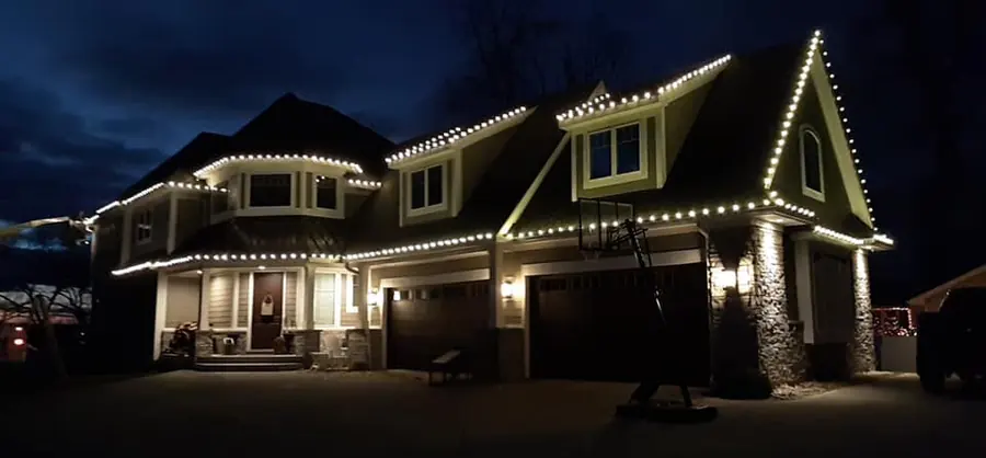 A large two story home at dusk with warm white bulbs outlining the rooflines, gables and dormers.